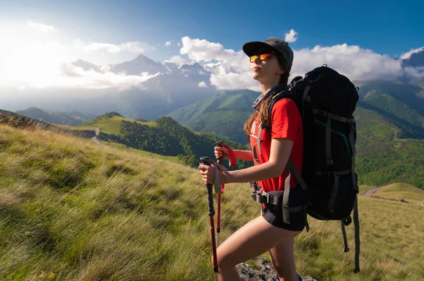 En turist flicka med en ryggsäck beundrar solnedgången från berget — Stockfoto