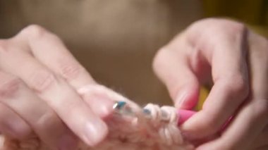 Yakın plan. Çekici beyaz bir kadının elleri, günlük giysiler içinde kanepede oturuyor ve bir örgü örerek yün bir ürün örüyor.