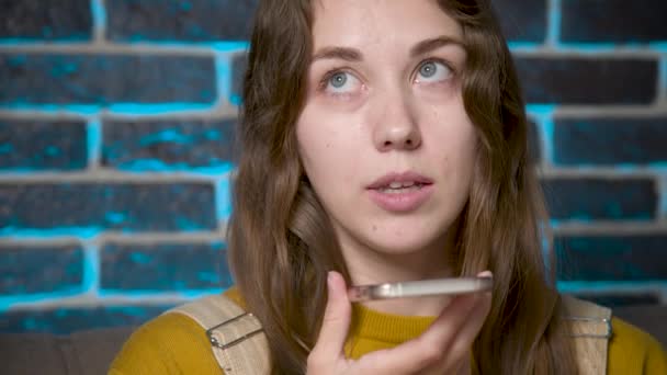 A friendly Caucasian girl uses a virtual assistant on her mobile phone. Smiling young white woman recording a reply to audio message on a social network. — Stockvideo