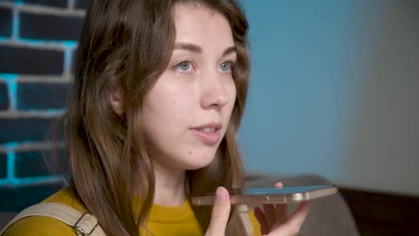 A friendly Caucasian girl uses a virtual assistant on her mobile phone. Smiling young white woman recording a reply to audio message on a social network. — Stock Video