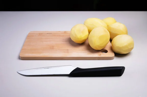 Mutfak bıçağının yanındaki tahta kesme tahtasındaki soyulmuş patatesler. Ev yapımı sebzeler. Sağlıklı yemek. — Stok fotoğraf