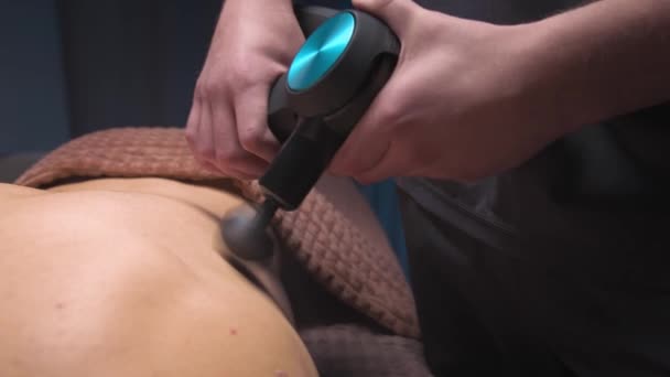 Elektrikli masaj aleti kullanarak perküsyon şok dalgası masajı. Profesyonel masaj odasında erkek bir sporcunun beline masaj yap. — Stok video