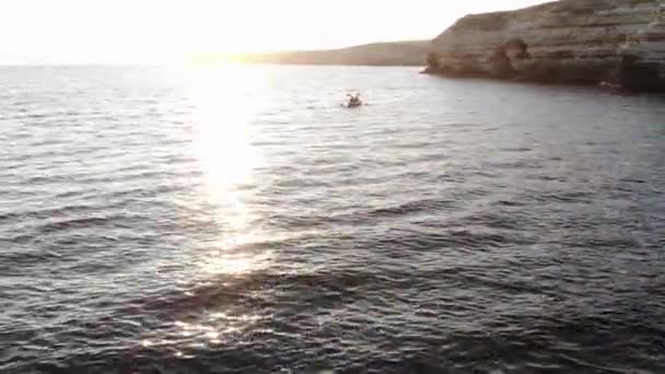 Aerial view of two people in a canoe float on the sea against the backdrop of a rocky coast with a cave. Twin kayaking at sea — Vídeo de Stock