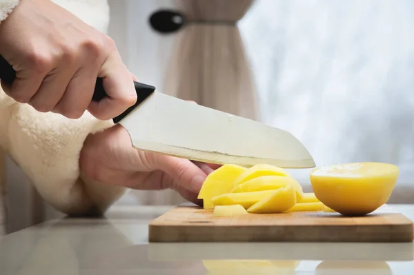 Крупный план женских рук, режущих свежий очищенный картофель на деревянной доске. Вегетарианская пища — стоковое фото