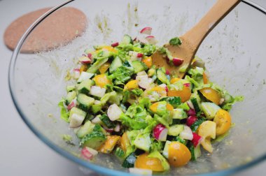 Tahta kaşıkla şeffaf bir kasede taze ve lezzetli sebzelerden oluşan taze bir vegan salatasının yakın çekimi. Detoks salata kasesi görünümü