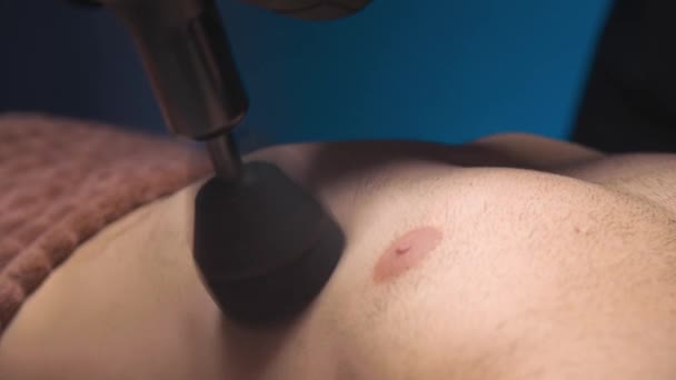 Close-up of a Caucasian male pectoral muscle percussion massager working out in a professional massage parlor — Stockvideo