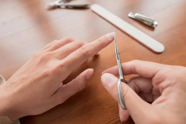 Primer plano de la mano de la mujer joven caucásica haciendo tijeras de manicura, corte de uñas en casa con suministros de uñas. — Foto de Stock