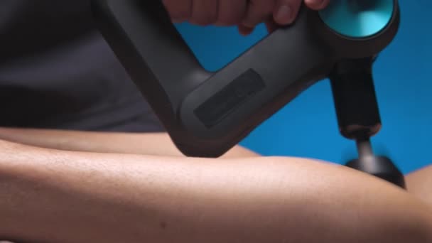 Close-up de um massagista masculino profissional estimula os músculos das pernas de um paciente masculino em uma sala de spa escura para massagem. Efeito mecânico da percussão nos músculos sobrecarregados — Vídeo de Stock