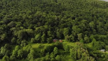 Hava manzaralı iki ahşap ev yeşil bir ormanla çevrili bir çimenlikte duruyor. Uzakta, dağlarda ekolojik yerleşim. Geri çekilmek ve küçülmek için modern yerler