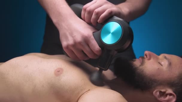 Primer plano de un masajeador masculino caucásico de percusión muscular pectoral que trabaja en una sala de masajes profesional — Vídeo de stock