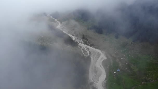 Letecký pohled na horskou řeku obklopenou zeleným alpským lesem za oblačného dne s mlhou a nízkými mraky. Nízký letový přehled mystického údolí 4k — Stock video