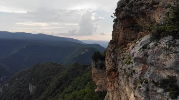 Vue aérienne volant à côté d'une falaise dans une vallée de montagne sur fond de collines et de rochers couverts de forêts verdoyantes — Video