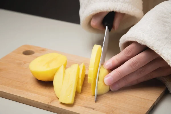 Primer plano de las manos femeninas cortando papas frescas peladas en una tabla de madera de corte. Preparación de alimentos vegetarianos — Foto de Stock