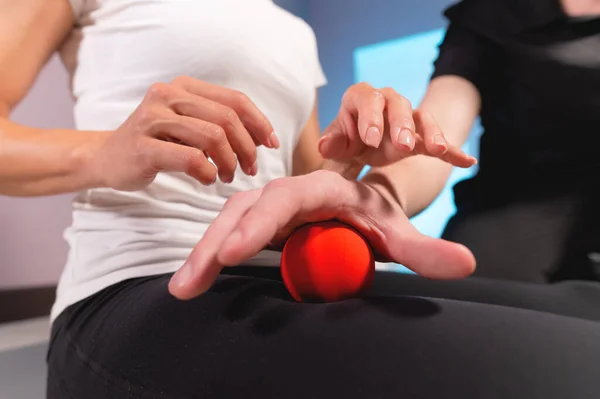 Primer plano de un masajista masculino que muestra a un cliente cómo usar y masajear una pelota. Masaje miofascial en el muslo — Foto de Stock