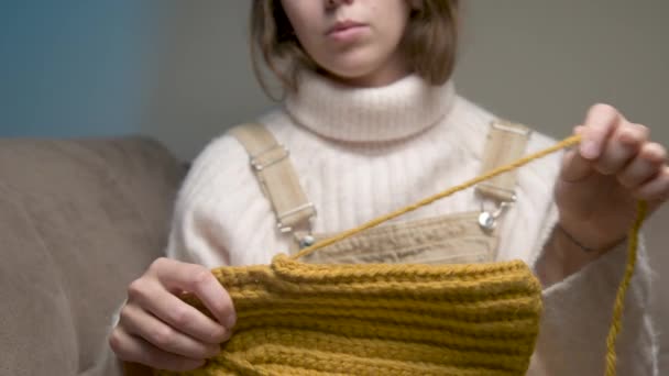 若い白人女性のクローズアップは、毛糸が毛糸製品を編んでいる間に間違いを犯すことを結ぶ — ストック動画