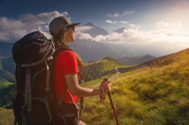 Güneş altında güneşli bir günde tepeye doğru yürüyen genç bir turist. Dağ manzarası çok güzel. Çekici yürüyüşçü sporcu kadın.