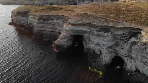 Vista aérea de um barco a motor com turistas navega para fora de uma caverna rochosa na costa do oceano à noite — Vídeo de Stock