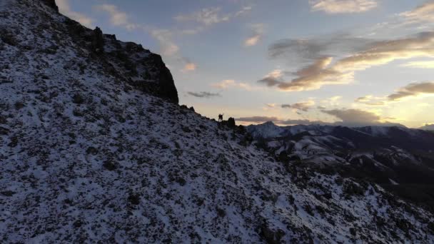 Letecký pohled na chodící pár oslavující úspěšný výstup na horu s rukama zvednutýma při krásném západu slunce. zasněžené hory — Stock video