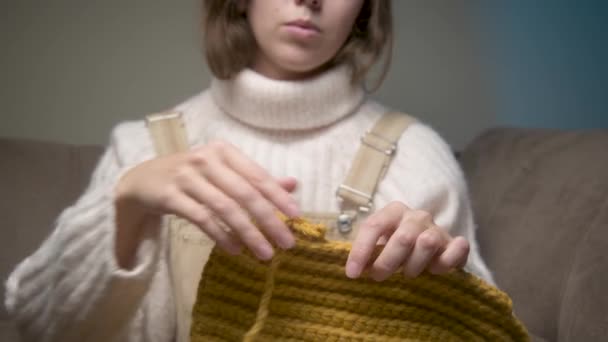 Κοντινό πλάνο των γυναικείων χεριών μιας Καυκάσιας νεαρής γυναίκας που ξετυλίγει ένα πλεκτό προϊόν. Οικιακά πλεκτά — Αρχείο Βίντεο