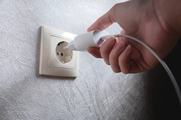 Bir kadının eli 220 voltluk elektrik prizine beyaz bir usb şarj aleti yerleştirirken yakın plan çekilmiş.
