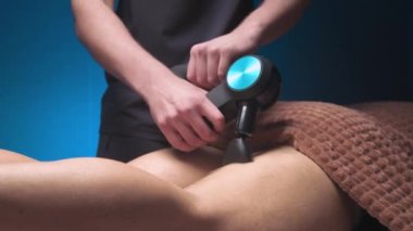 Erkek masör, erkek bir müşteriye perküsyon vibratörlü masaj aleti yardımıyla kalçalara masaj yapıyor. Atletik vücut masajı için şok terapisi..