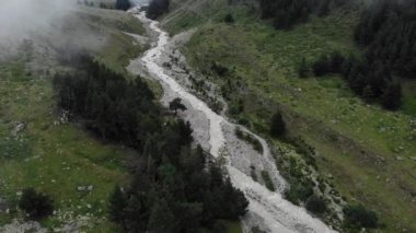 Küçük çalkantılı bir dağ nehri bulutlu bir havada taşların üzerinden akar, yemyeşil bitki örtüsüyle çevrili. Mistik havanın havadan görünüşü.