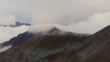 Dağlarda bulutların hareketinin akşam vakti hızlandırılması. Dağ tepeleri ve tepelerin üzerinden taşan bulutlar. Hava görüntüsü. İklim değişikliği. Küresel sıcaklık