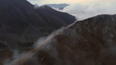 Dağlarda bulutların hareketinin akşam vakti hızlandırılması. Dağ tepeleri ve tepelerin üzerinden taşan bulutlar. Hava görüntüsü. İklim değişikliği. Küresel sıcaklık