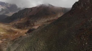 Taçlı siyah atlar bulutlu bir havada dağ geçidinde yeşil bir çayırda otlarlar. Hava görünümü