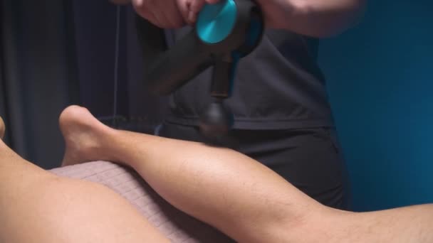 Professionele masseur man doet massage oefeningen van de kroon spier aan de klant met behulp van een percussie vibro massager. Shock therapie voor een regenererende massage van het atletische lichaam. — Stockvideo