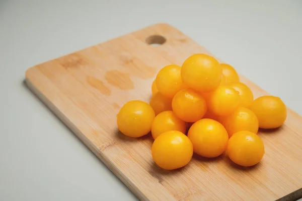 Mutfaktaki tahta kesme tahtasının üzerinde beyaz bir masanın üzerinde sarı kiraz domatesleri yığını. — Stok fotoğraf