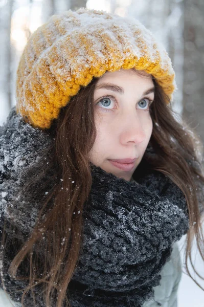 Retrato de una joven mujer caucásica sonriente en un sombrero de lana brillante y bufanda, en el contexto de un bosque cubierto de nieve. — Foto de Stock