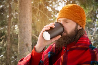 Şapkalı ve ekoseli sakallı adamlar ormanın arka planında içki içiyorlar.