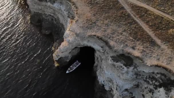 Luchtfoto van een motorboot met toeristen zeilen uit een rotsachtige grot aan de kust van de oceaan in de avond — Stockvideo