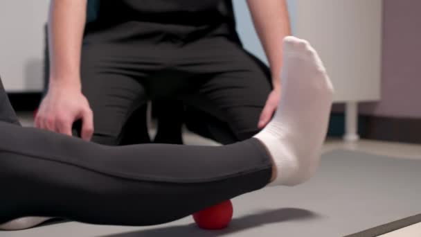 Närbild Ung manlig massageterapeut lär klient Kaukasiska kvinna patient myofascial själv massage av ben och höfter med hjälp av massage boll inomhus. Myofaskulär frisättning — Stockvideo