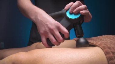 Erkek masör, erkek bir müşteriye perküsyon vibratörlü masaj aleti yardımıyla kalçalara masaj yapıyor. Atletik vücut masajı için şok terapisi..