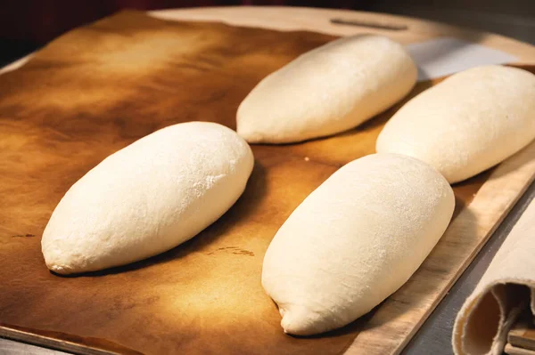 Kilka surowych bochenków francuskiego chleba leży na drewnianej desce. Przygotowanie przed pieczeniem chleba rzemieślniczego — Zdjęcie stockowe