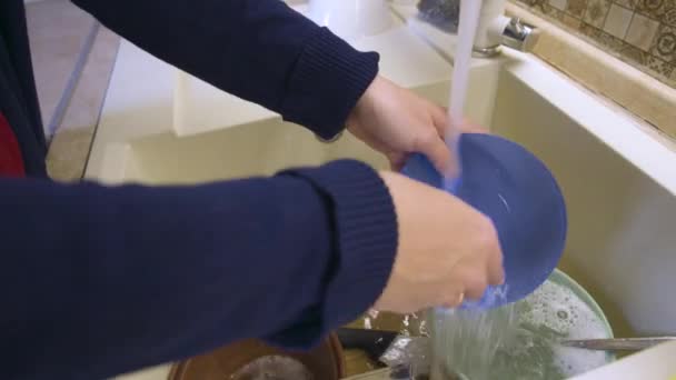 Una ama de casa lava platos sucios bajo el agua corriente en un fregadero en una cocina moderna. vida en casa — Vídeo de stock