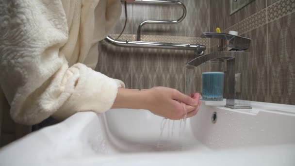 Μια καυκάσια όμορφη γυναίκα πλένει το πρόσωπό της κάτω από τρεχούμενο νερό στο μπάνιο του σπιτιού. Φροντίδα του δέρματος, θεραπείες ομορφιάς στο σπίτι, καθαριότητα και υγιεινή έννοια. — Αρχείο Βίντεο