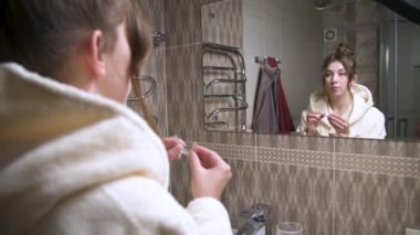 Genç bir kadın, banyo aynasına bakarken üst dişlerini düzeltmek için alt dişlerine düzenleyici bir sabitleyici takıyor. Düzeltmek için alt dişlere hizalayıcı kurulumu