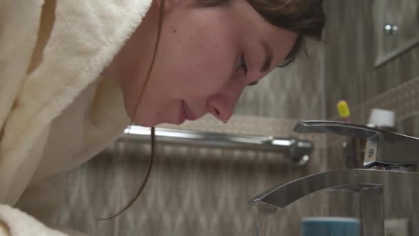 Közelkép, fehér, gyönyörű nő mossa az arcát a folyóvíz alatt egy otthoni fürdőszobában. Bőrápolás, otthoni szépségápolás, tisztaság és higiénia. — Stock videók