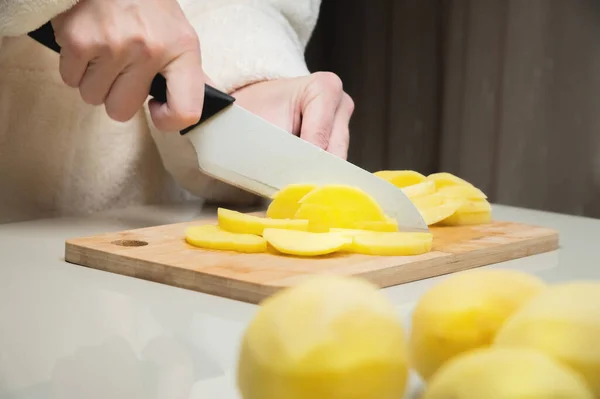 Joven mujer caucásica en un albornoz se para y corta patatas en una tabla de cortar — Foto de Stock