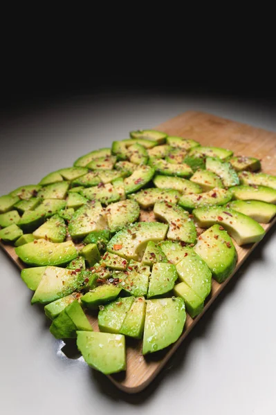 Brett vinkel Stora skivor av skivade mogna avokado ligger strukturerade på en träskärbräda. Strödd med kryddor. Friska livsmedel. Vegetarianism — Stockfoto