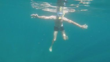 Kafkas sakallı, şnorkel takmış bir adam denizin altında sığ sularda serbest dalış yapıyor. Güneşli bir günde şnorkelle yüzmek