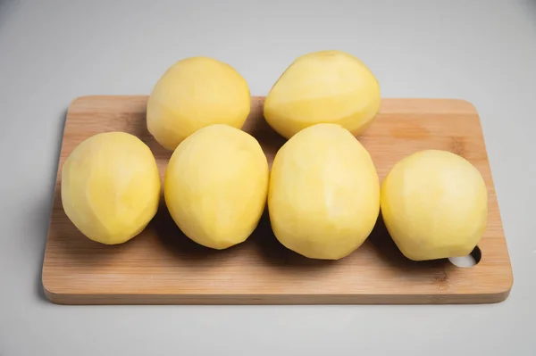 Zbliżenie Kilka obieranych ziemniaków na drewnianej desce do krojenia na białym stole. — Zdjęcie stockowe