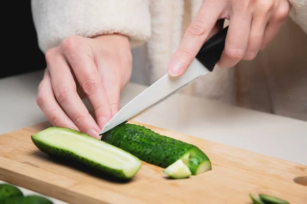 Close-up of female hands cutting fresh cucumbers on a wooden cutting board — Stock Photo, Image