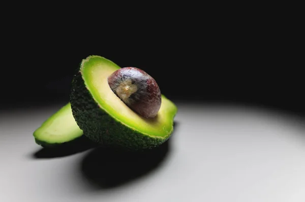 En halv avokado med en grop på ett vitt bord. kontrastskott mjuk fokus — Stockfoto