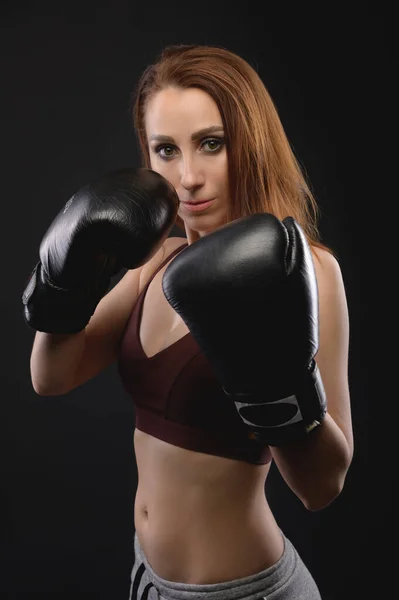 Сильная и строгая белая женщина-боец в спортивной одежде и боксерских перчатках на черном фоне. Феминизм и боевые виды спорта — стоковое фото