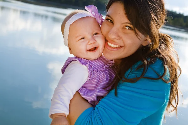 Mãe e bebê filha sorrindo perto de um lago — Fotografia de Stock