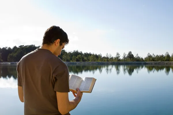 Hombre leyendo la Biblia por el lago — Foto de Stock